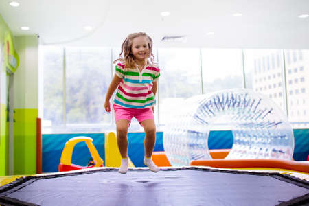 Child jumping on colorful playground trampoline. Kids jump in inflatable bounce castle on kindergarten birthday party Activity and play center for young child. Little girl playing indoor.の写真素材