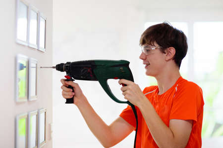 Man drilling wall. Home renovation and decoration. Young male adult with perforator, hammer and screwdriver hanging photo frame in new house. Drill work.の写真素材