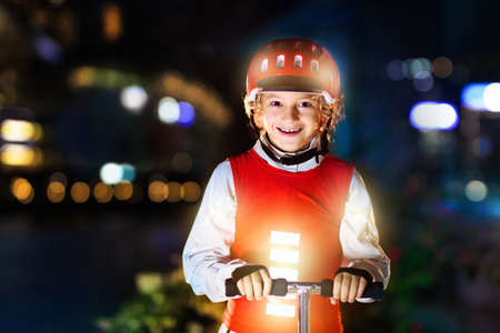 Kid in reflective vest in darkness. Safety on dark city streets for school children. Safe way home at night or in the evening. Fluorescent stripes on kids clothing and backpack. Boy walking at dusk.の写真素材