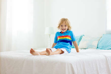 Child playing in bed in white sunny bedroom with window. Kids room and interior design. Baby boy at home. Bedding and textile for children nursery. Kid with toy and book. Nap and sleep time.の写真素材