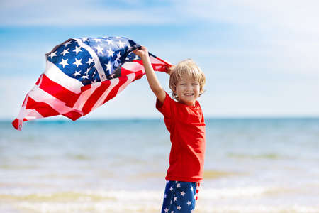 Kids run with USA flag on sunny beach. 4th of July celebration. American family fun on Independence Day weekend. Patriotic children celebrate US holiday. Boy and girl with symbols of America.の写真素材