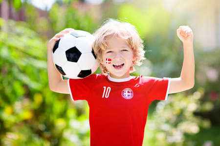 Denmark football fan cheering. Danish kids play soccer and celebrate victory on outdoor field. Danmark team supporter. Little boy in Dansk flag jersey kicking ball. Sports training for children.の写真素材