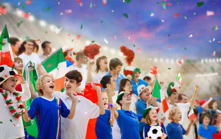Italy football supporter on stadium. Italian fans on soccer pitch watching team play. Group of supporters with flag and national jersey cheering for Italia. Championship game. Forza azzurriの写真素材