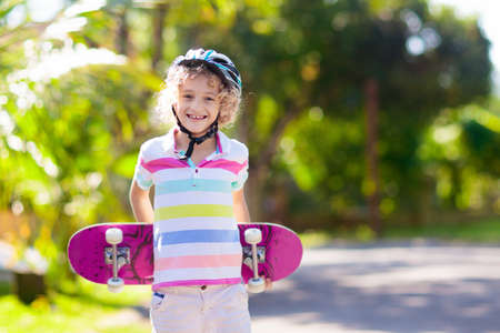 Kid with skateboard. Child riding skate board. Healthy sport and outdoor activity for school kids in summer. Sports fun. Helmet for safe exercise. Boy skater in sunny park. Children training.の写真素材