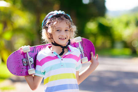 Kid with skateboard. Child riding skate board. Healthy sport and outdoor activity for school kids in summer. Sports fun. Helmet for safe exercise. Boy skater in sunny park. Children training.の写真素材