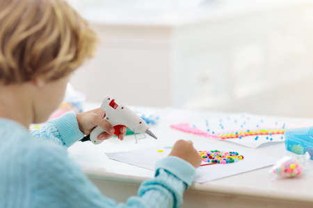 Crafts for kids. Child with hot glue gun. Creative little boy sticking buttons and beads in rainbow design. Art and creativity class in school or kindergarten. Preschool kid with fun diy project.の写真素材