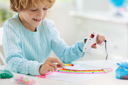 Crafts for kids. Child with hot glue gun. Creative little boy sticking buttons and beads in rainbow design. Art and creativity class in school or kindergarten. Preschool kid with fun diy project.の写真素材