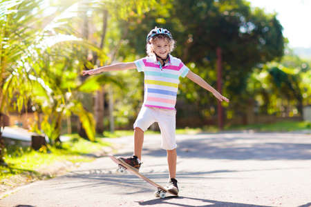 Kid with skateboard. Child riding skate board. Healthy sport and outdoor activity for school kids in summer. Sports fun. Helmet for safe exercise. Boy skater in sunny park. Children training.の写真素材
