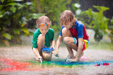 Kids playing in the rain. Chalk drawing fun. Art and crafts for young children. Boys experiment with watercolor in heavy shower outdoor in garden patio. Healthy activity on rainy autumn day.の写真素材