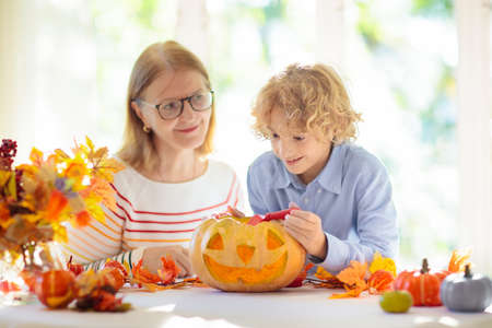 Family carving pumpkin for Halloween celebration. Boy and girl child cutting jack o lantern for traditional trick or treat decoration. Kids decorate home. Children carve pumpkin. Spooky Halloween fun.