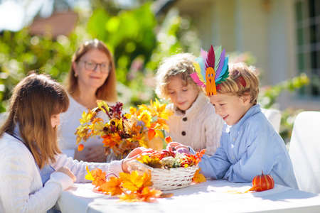 Family celebrating Thanksgiving. Kids autumn arts and crafts. Little boy with pumpkin and turkey hat at decorated table. Happy celebration on sunny fall day. Child decorating home.の写真素材