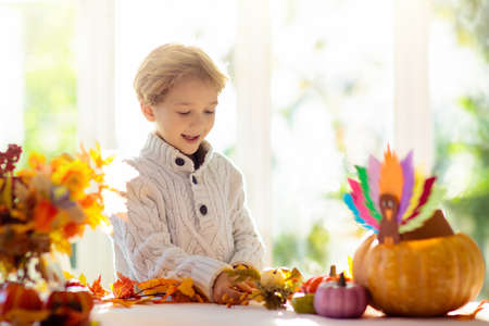 Family celebrating Thanksgiving. Kids autumn arts and crafts. Little boy with pumpkin and turkey hat at decorated table. Happy celebration on sunny fall day. Child decorating home.の写真素材