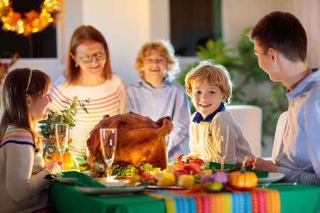 Family at Thanksgiving dinner. Parents, grandparents and kids enjoy roasted turkey and vegetable meal. Children and grandmother say a thankful prayer. Festive home decoration and table setting.の写真素材