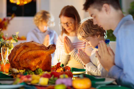 Family at Thanksgiving dinner. Parents, grandparents and kids enjoy roasted turkey and vegetable meal. Children and grandmother say a thankful prayer. Festive home decoration and table setting.の写真素材