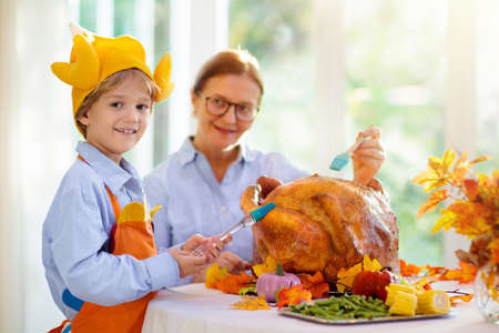 Turkey for Thanksgiving. Family cooking festive dinner. Grandmother and child roast meat in decorated kitchen. Mother and kid cook in autumn. Grandparents visit. Fall season food.の写真素材