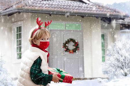 Child in face mask with Christmas present at decorated house door. Kid wearing protective mask for safe Xmas celebration.の写真素材