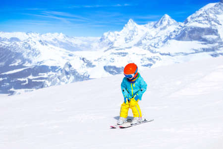 Child skiing in the mountains. Kid in ski school. Winter sport for kids. Family Christmas vacation in the Alps. Children learn downhill skiing. Alpine ski lesson for boy or girl. Outdoor snow fun.の写真素材