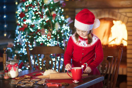 Child baking Christmas cookies at fire place and decorated tree. Kids bake Xmas sweets. Family with kids celebrating Christmas at home. Little girl cooking in the kitchen. Winter fun for children.の写真素材