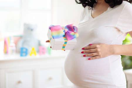 Baby shower or gender reveal party. Pregnancy celebration with friends. Young pregnant Asian woman holding gifts for newborn. Pink and blue decoration for baby girl or boy. Maternity event.の写真素材