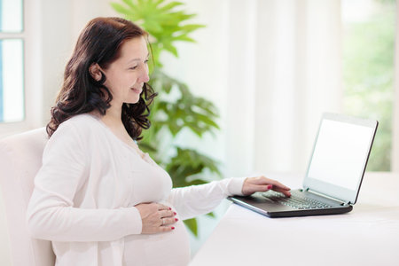 Pregnant woman at laptop. Pregnancy online shopping. Asian expecting mom buying baby stuff in web...