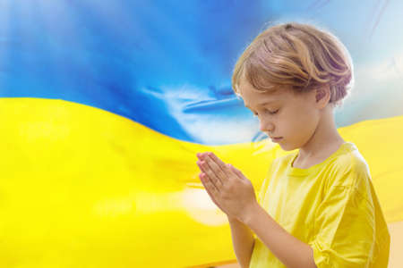 Pray for Ukraine. Child with Ukrainian flag. Little blond boy waving national flag praying for peace. Happy kid celebrating Independence Day.の写真素材