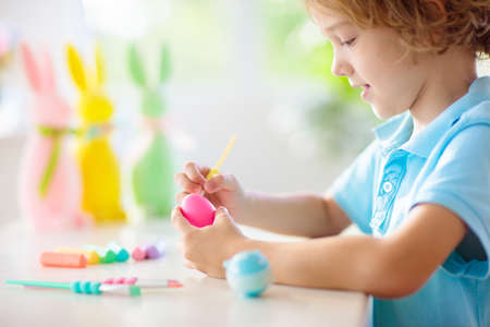 Kids dyeing Easter eggs. Children in bunny ears dye colorful egg for Easter hunt. Home decoration...