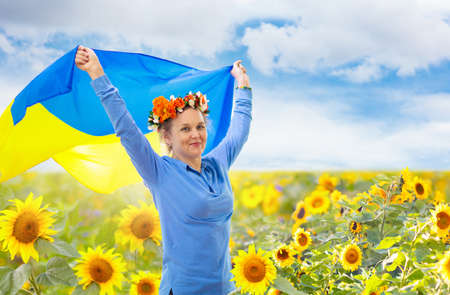 Pray for Ukraine. Woman with Ukrainian flag in sunflower field. Happy female waving national flag praying for peace. Cheering girl with flower crown celebrating Independence Day.の写真素材