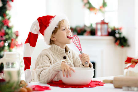 Family baking Christmas cookies. Children bake gingerbread man pastry licking whisk. Kids Xmas fun. Little boy in Santa hat making dough for winter cookie. Home holiday decoration.の写真素材