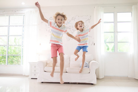 Kids play at home. Children jump, run and dance. Active boys playing tag, running and jumping on couch in white sunny house. Family indoor fun. boy in living room. Activity and movement indoors.の写真素材