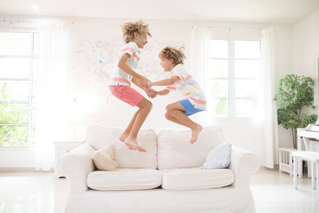 Kids play at home. Children jump, run and dance. Active boys playing tag, running and jumping on couch in white sunny house. Family indoor fun. boy in living room. Activity and movement indoors.の写真素材