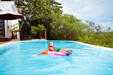 Child with goggles in swimming pool. Little girl learning to swim and dive in outdoor pool of...