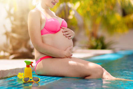 Pregnant woman in swimming pool. UV sun protection cream for skin. Sunscreen for safe tan. Healthy and active pregnancy. Young mom on tropical vacation. Swim holiday and water fun for mom and baby.の写真素材