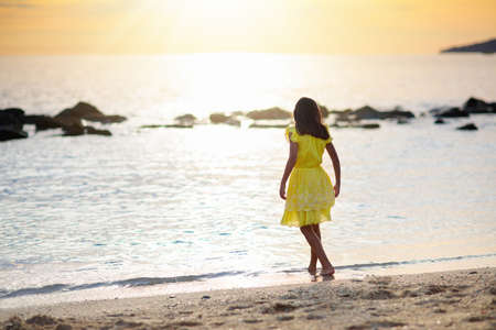 Little girl playing on tropical beach. Children play on the beach. Water and sand fun. summer holidays. Travel with kids. ocean holiday with child. Sunset walk at the beach.の写真素材