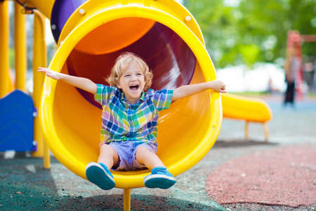 Child playing outdoor playground. Kids play on school or kindergarten yard. Active kid on colorful slide and swing. Healthy summer activities for children. Little boy climbing outdoors.の写真素材