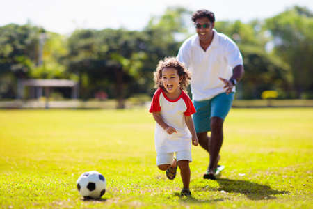 father and son play football. Dad and little boy play soccer. Young active family enjoy sunny summer day outdoor. Healthy sport for kids. football game club.の写真素材