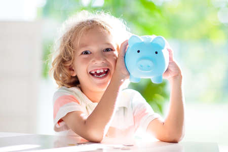 Child putting coin in piggy bank. Kids learn about money. Savings and investment. Little boy saving cash. Wealth growth for young family with children. Budget planning at home.の写真素材