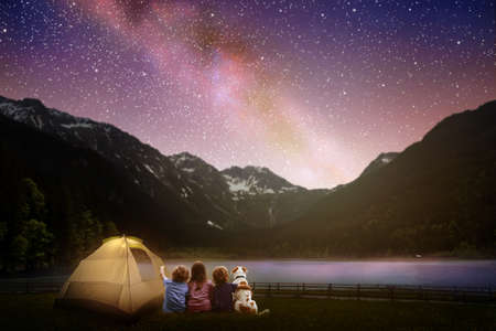 Family camping under starry night sky. Milky way watching. Camp bonfire with kids. Travel and hiking...