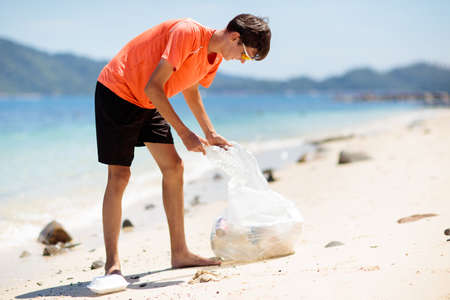 plastic garbage. Sea and ocean pollution. Beach cleanup. Young man picking used plastic bottles on sand shore. Environmental activist collecting rubbish. Save our earth. nature protection.の写真素材