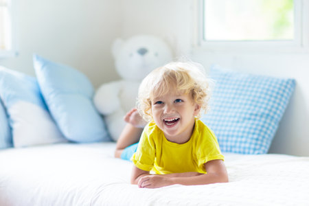 Child playing in bed in white sunny bedroom with window. Kids room and interior design. baby boy at home. Bedding and textile for children nursery. Kid with toy and book. Nap and sleep time.の写真素材
