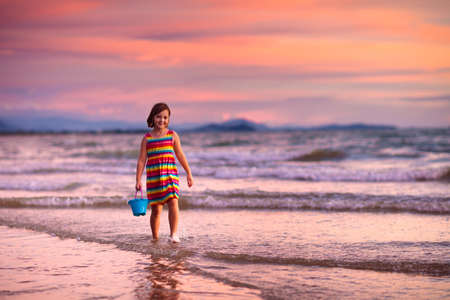 child playing on ocean beach. Kid jumping in the waves at sunset. Sea vacation for family with kids. Little girl running on tropical beach of exotic island during summer holiday.の写真素材