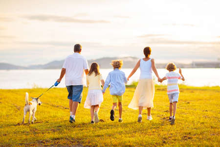 Family with kids running outdoors at sunset. Parents and children walking dog at the beach. Summer...