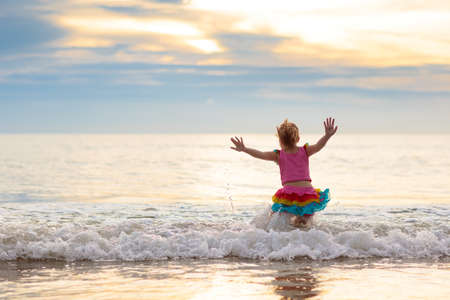 Child playing on ocean beach. Kid jumping in the waves at sunset. Sea vacation for family with kids. Little girl running on tropical beach of exotic island. summer holiday. Swimwear for kidsの写真素材