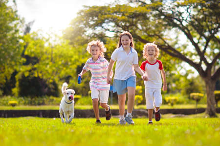 Family with kids running outdoors on sunny summer day. Siblings play in a garden. Kid boy and girl walking dog in a park. Vacation with child and pet. Group of school kids run with a puppy.の写真素材