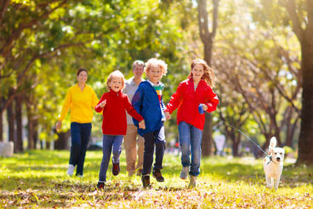Family walking in autumn park. Kids play in sunny forest. outdoor fun. Mother, father and children walk the dog on sunny warm fall day. Boy and girl in rain jacket. Parents with son and daughter.の写真素材