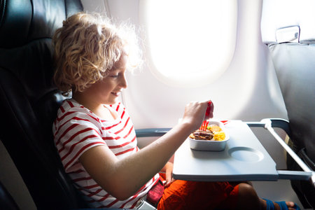 child in airplane window seat. Kids flight meal. children fly. Special inflight menu, food and drink for baby and kid. Boy eating healthy lunch in airplane. Travel and family vacation.の写真素材