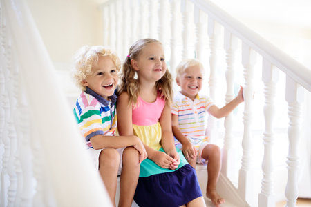 Kids walking stairs in white house. Children playing in sunny staircase. family moving into new home. Boy and girl on steps of modern stairs. Foyer and living room interior. Child at stair case.の写真素材