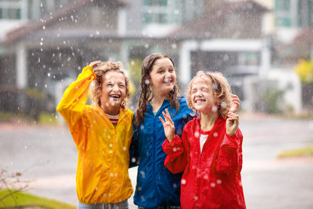 Kids play in heavy autumn rain. Children walk on city street in cold rainy weather. Waterproof warm outdoor wear. Boy and girl with colorful umbrella and rain jackets. Outdoor fun.の写真素材