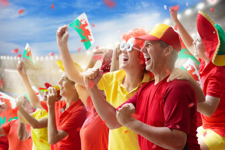 Wales fans on stadium. Welsh supporters. Crowd cheering for Wales football team victory. Soccer match on outdoor pitch. Patriotic party with national flag and jersey.の写真素材