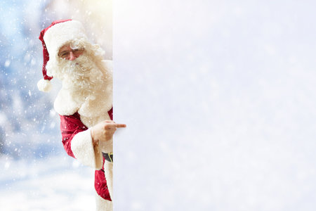 Santa in snowy forest pointing at empty cope space for your text. Merry Christmas card or advertisement template. Santa Claus list of presents and gifts. Xmas shopping promotion.の写真素材