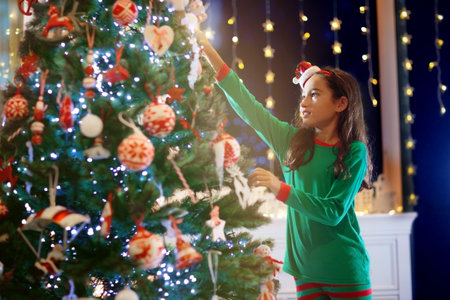 Child at Christmas tree and fireplace on Xmas eve. Family with kids celebrating Christmas at home. Little girl decorating xmas tree and opening presents. Gifts for winter holidays at fire place.の写真素材